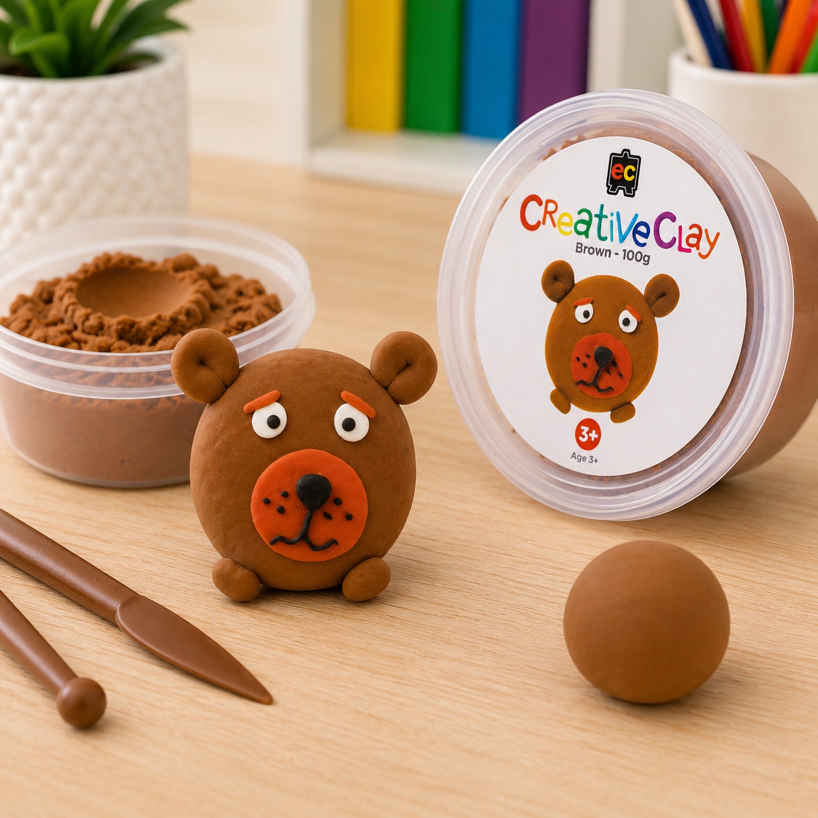 CreativeClay Brown 100g packaging displayed alongside a finished bear model, sculpting tools and an open tub of clay. The image showcases the product branding, colour accuracy and creative applications for classrooms, art rooms and home craft environments.
