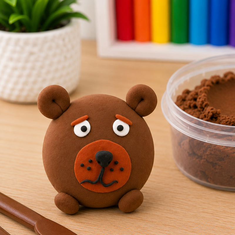 Detailed bear sculpture made from brown CreativeClay positioned beside an open container of clay and modelling tools. The image demonstrates the clay's flexibility, soft consistency and ability to create expressive characters with fine details and rounded shapes.