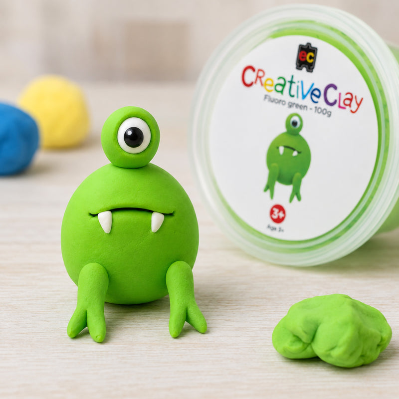 Bright fluoro green CreativeClay 100g displayed as a smooth clay sphere on a tabletop beside an open container of clay. Additional colourful clay pieces appear in the background, highlighting the vibrant colour intensity and soft texture suitable for creative modelling projects.
