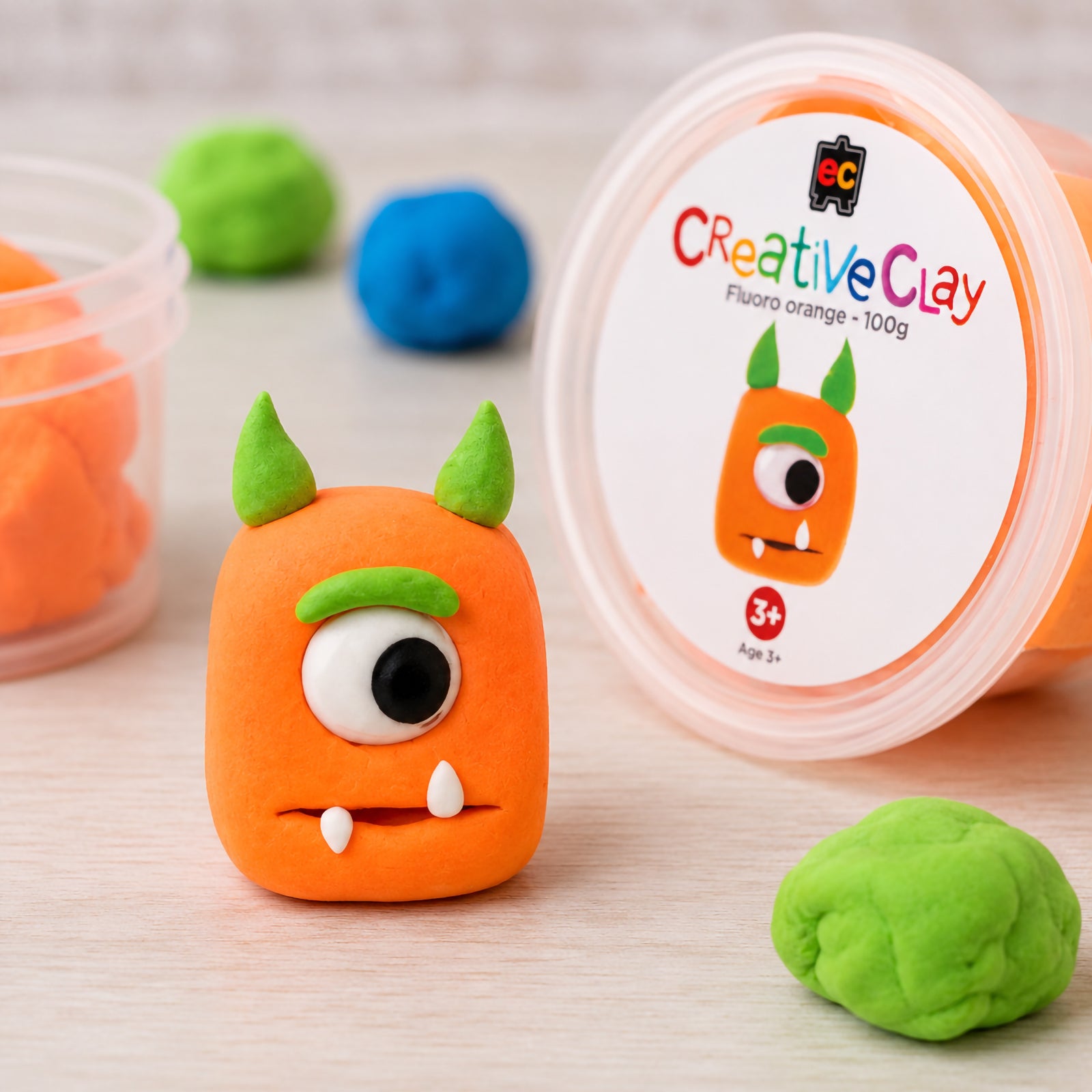 Completed monster sculpture positioned beside Educational Colours CreativeClay Fluoro Orange 100g packaging and additional clay pieces. This image highlights the vibrant colour, lightweight modelling properties and suitability for educational activities, creative play and decorative craft projects.