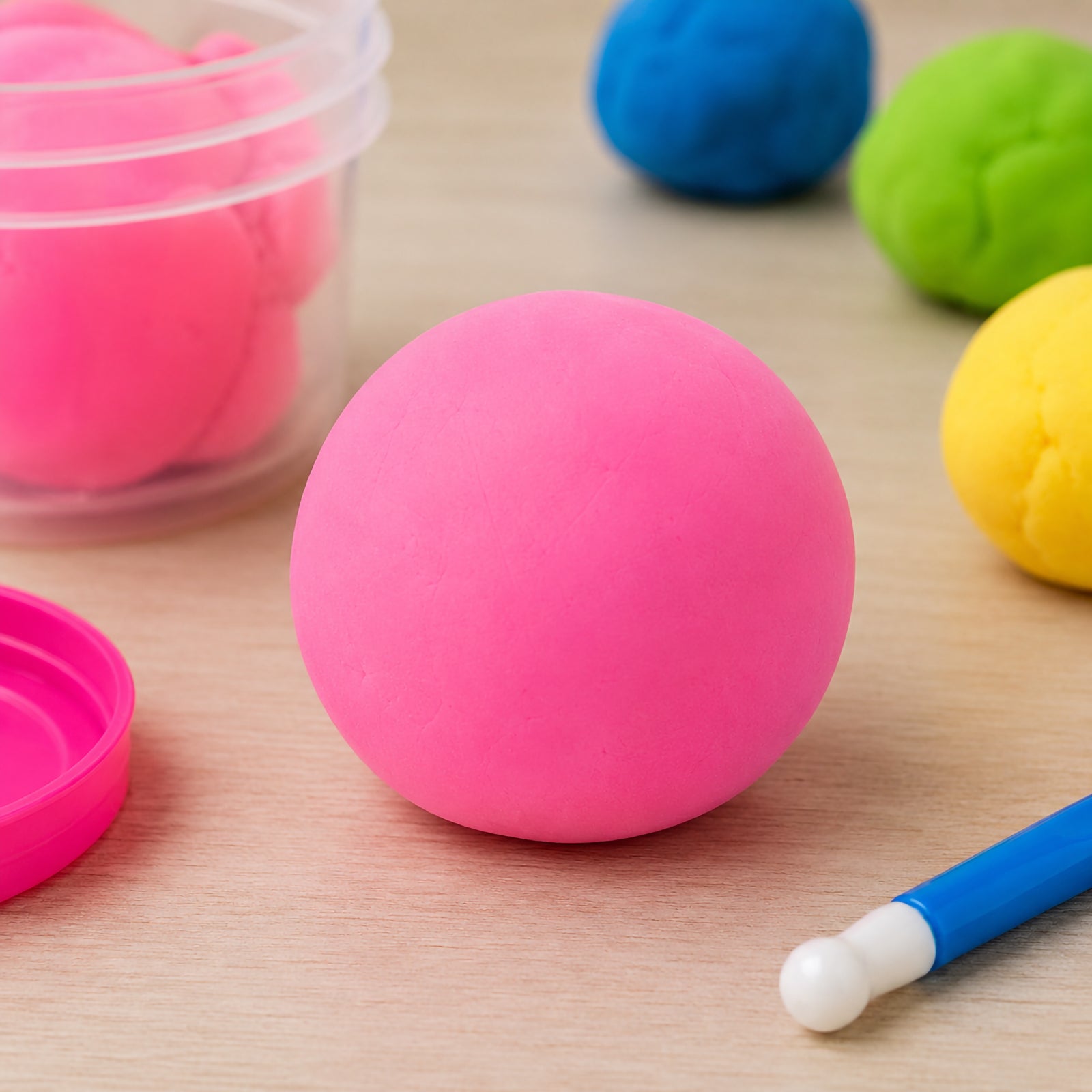 Bright fluoro pink ball of CreativeClay displayed on a tabletop beside an open container and modelling tool. The vivid fluorescent colour stands out against other clay colours in the background, highlighting the smooth texture and easy to shape consistency suitable for creative projects and classroom activities.