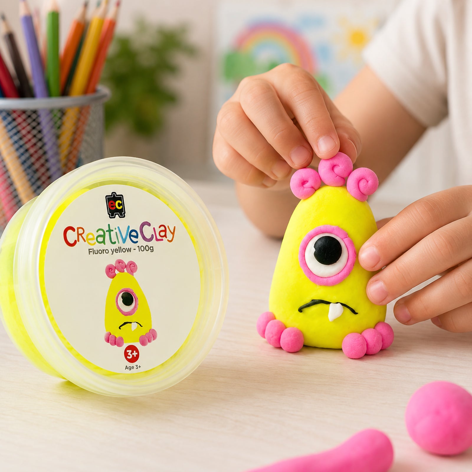 Child shaping a bright yellow clay creature beside an Educational Colours CreativeClay Fluoro Yellow 100g container. The image showcases hands on learning, creative play, fine motor skill development and the clay's ease of use for young artists.