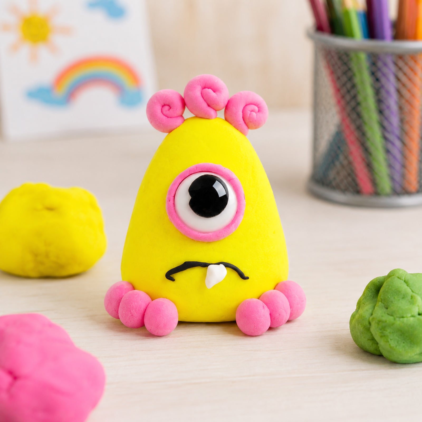 Cute one eyed yellow clay character decorated with pink accents and crafted from CreativeClay. The playful figure demonstrates the clay's flexibility, smooth finish and ability to create detailed characters, imaginative creatures and engaging classroom art projects.
