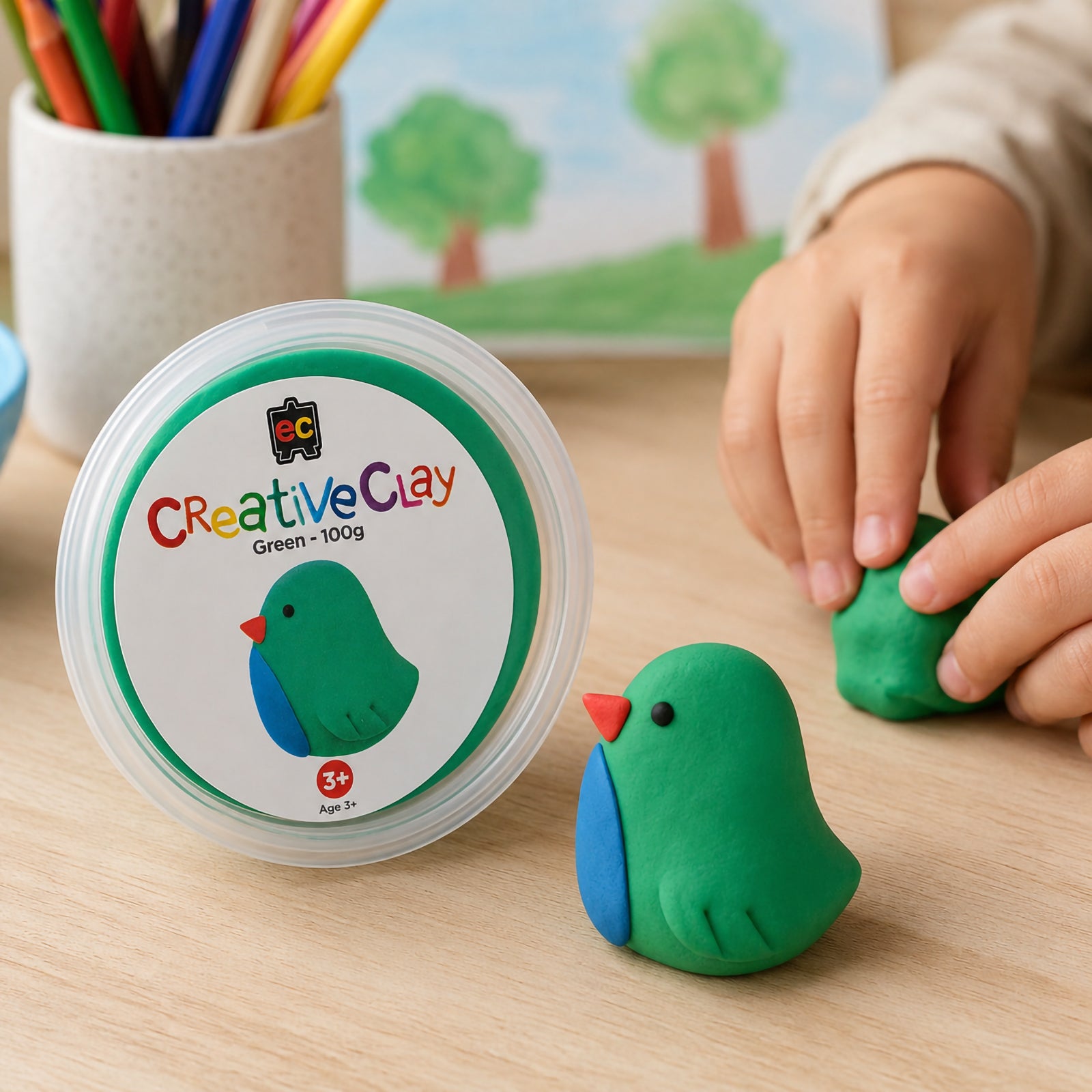 Educational Colours CreativeClay Green 100g container displayed beside a finished bird model while a child shapes clay in the background. The scene showcases classroom creativity, hands on learning and artistic exploration through modelling activities.