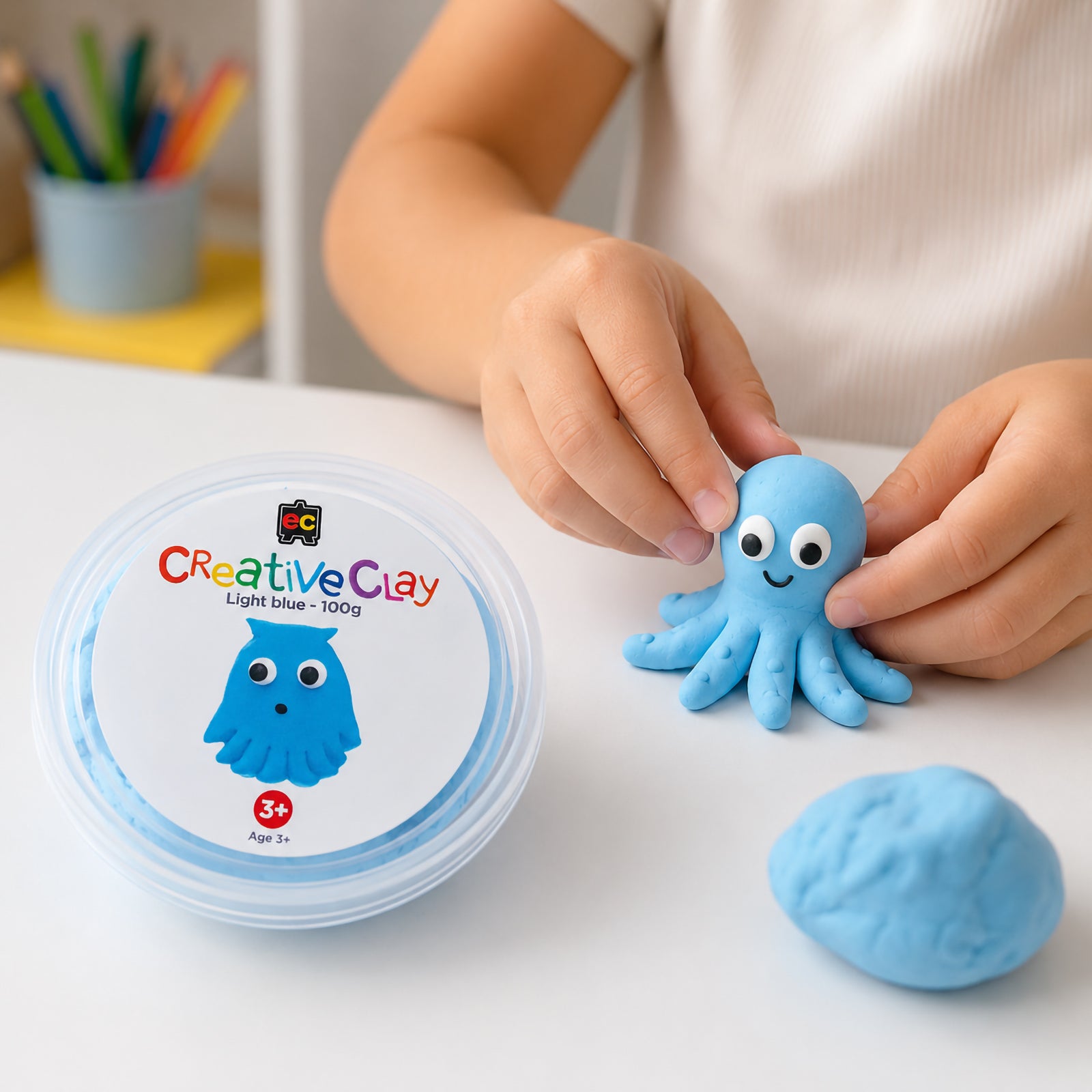 Educational Colours CreativeClay Light Blue 100g container displayed beside a completed octopus model while a child carefully adds finishing details. The scene showcases hands on learning, creativity and the clay's suitability for imaginative classroom and home projects.