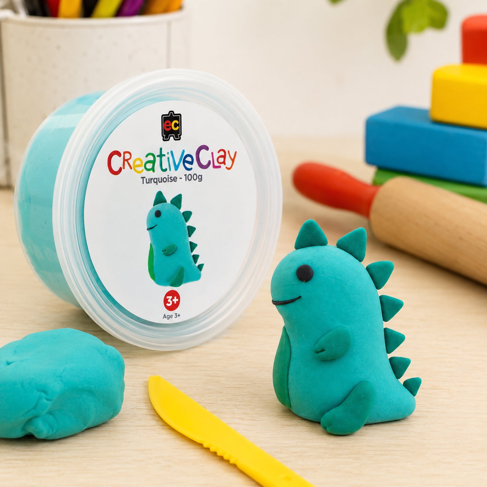 Educational Colours CreativeClay Turquoise 100g container displayed with a completed dinosaur sculpture, modelling tools and classroom craft materials. The image showcases product packaging and creative inspiration for learning environments.
