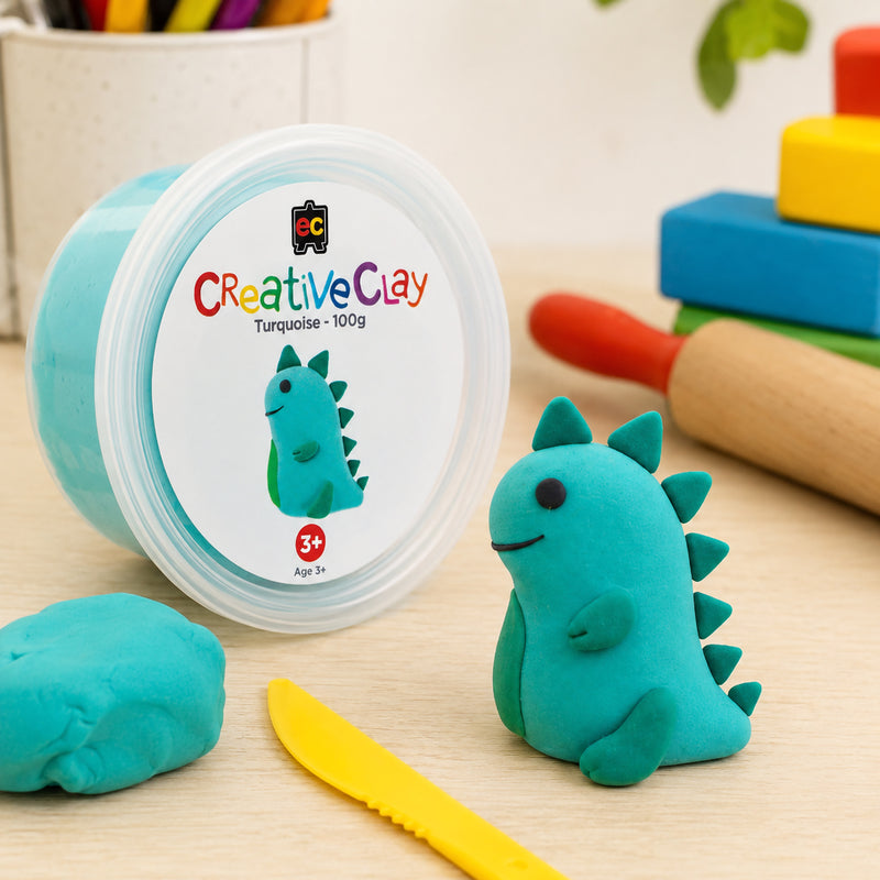 Educational Colours CreativeClay Turquoise 100g container displayed with a completed dinosaur sculpture, modelling tools and classroom craft materials. The image showcases product packaging and creative inspiration for learning environments.