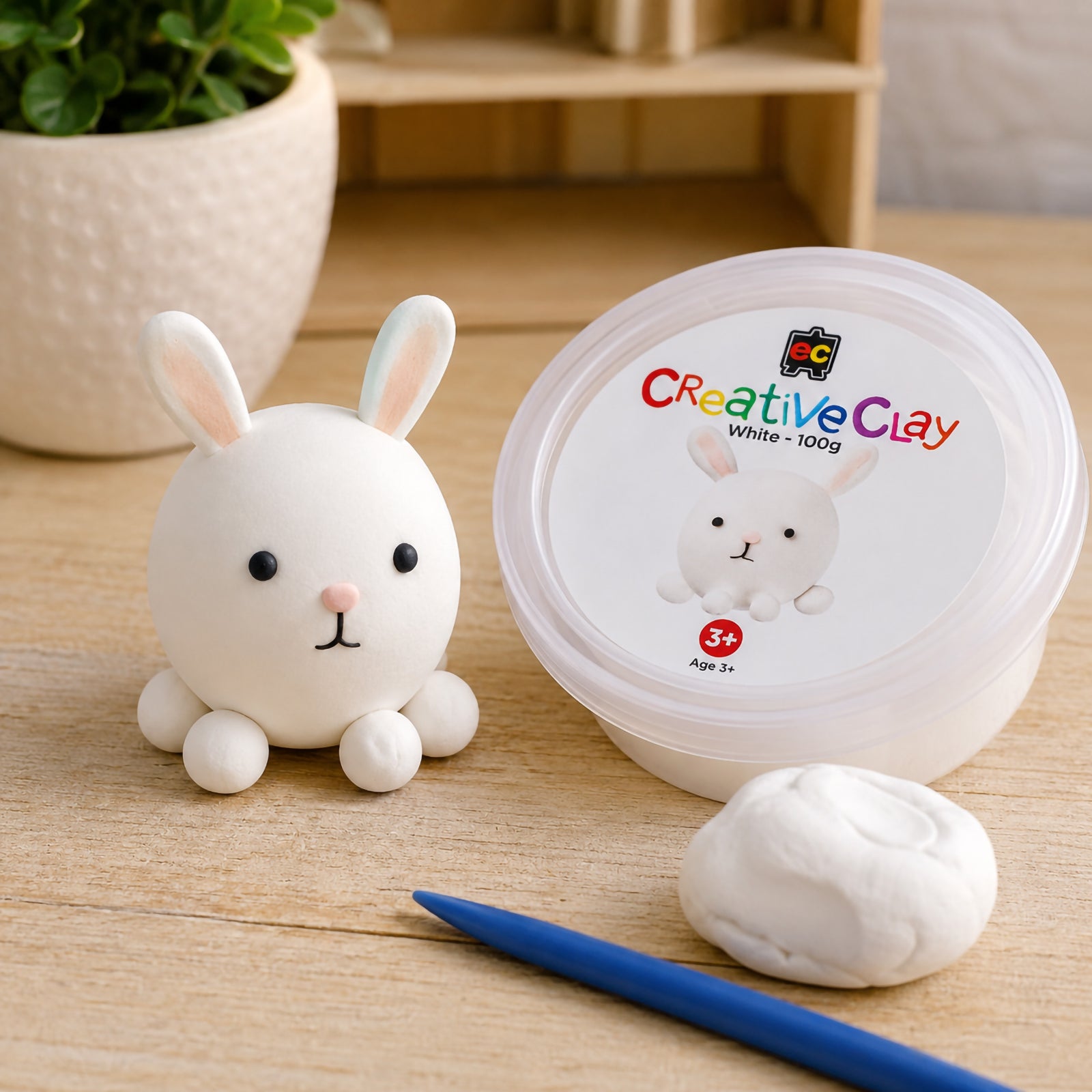 Educational Colours CreativeClay White 100g container displayed alongside a completed rabbit figure, modelling tool and clay sample. The scene showcases product packaging and creative possibilities for classrooms and home craft spaces.