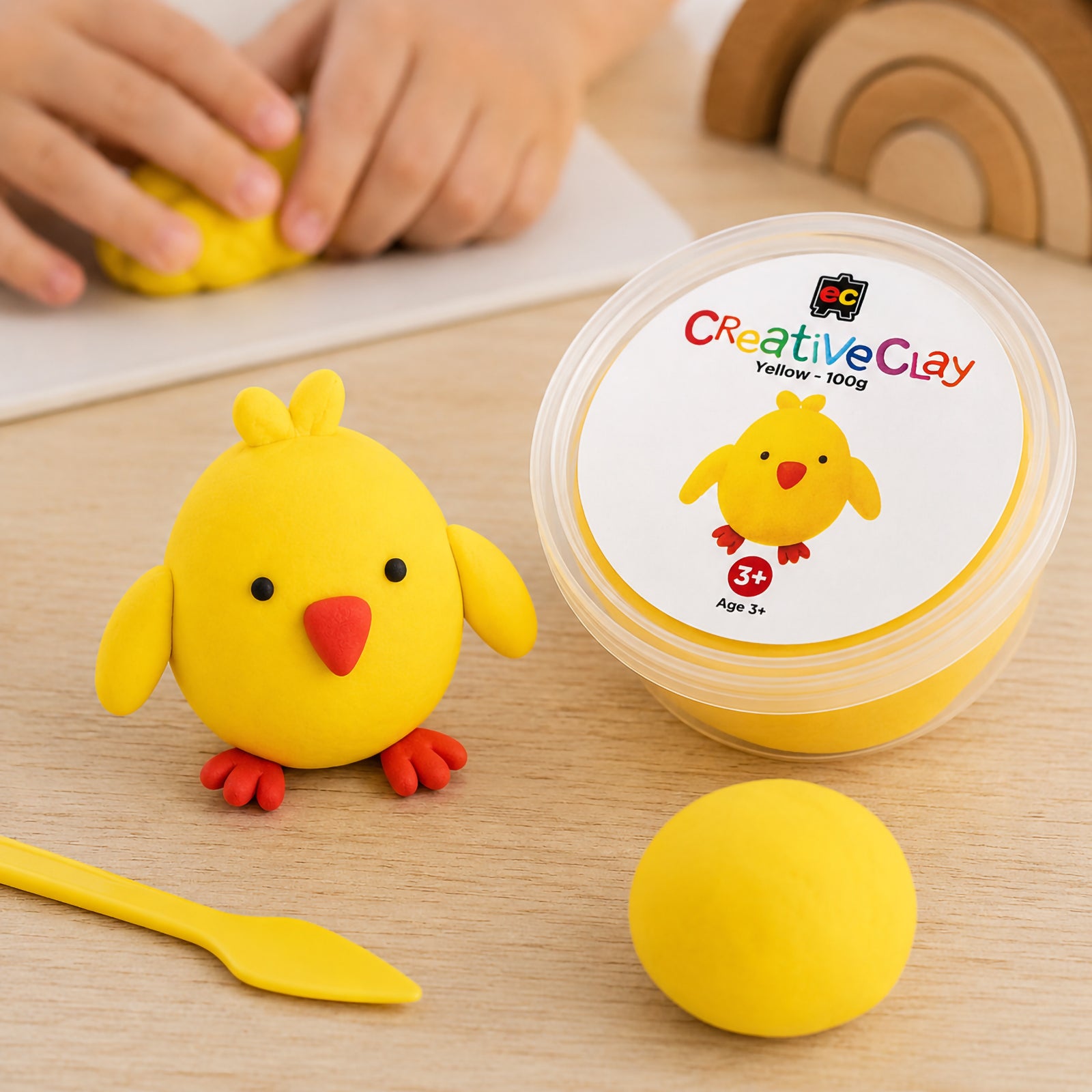 Educational Colours CreativeClay Yellow 100g container displayed beside a completed chick model, sculpting tool and clay sample. The image showcases the packaging and illustrates how the clay can be transformed into colourful handcrafted creations.