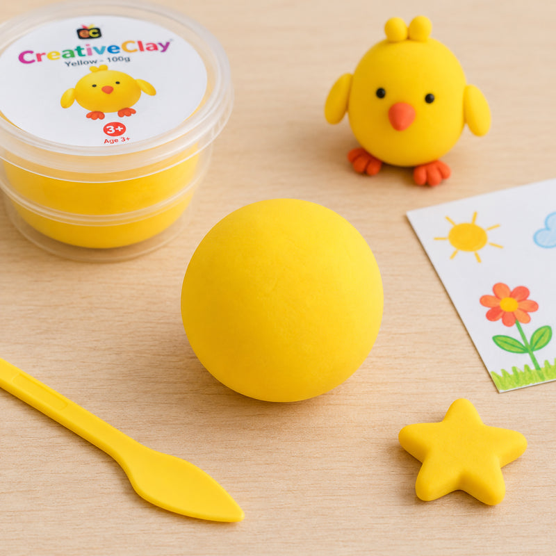 Bright yellow CreativeClay formed into a smooth ball on a craft table alongside a yellow modelling tool, star shape and cheerful chick figure. The scene highlights the vibrant colour, soft texture and creative possibilities of the air dry clay for educational and craft activities.