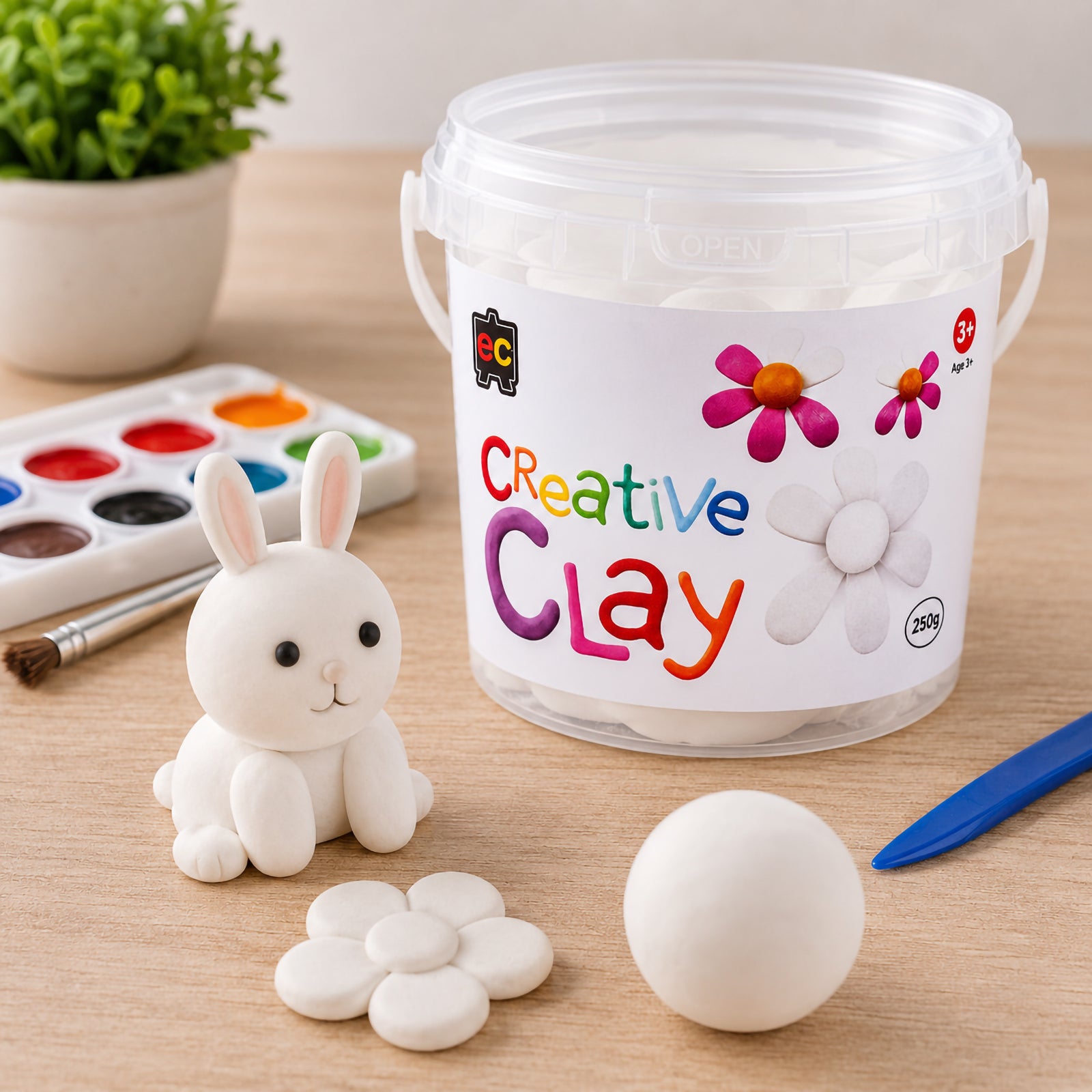 White rabbit figure handcrafted from CreativeClay positioned beside the 250g container, flower design and modelling tools. The image demonstrates the clay's ability to hold detailed shapes and create clean, professional looking sculptures suitable for classroom and home art projects.