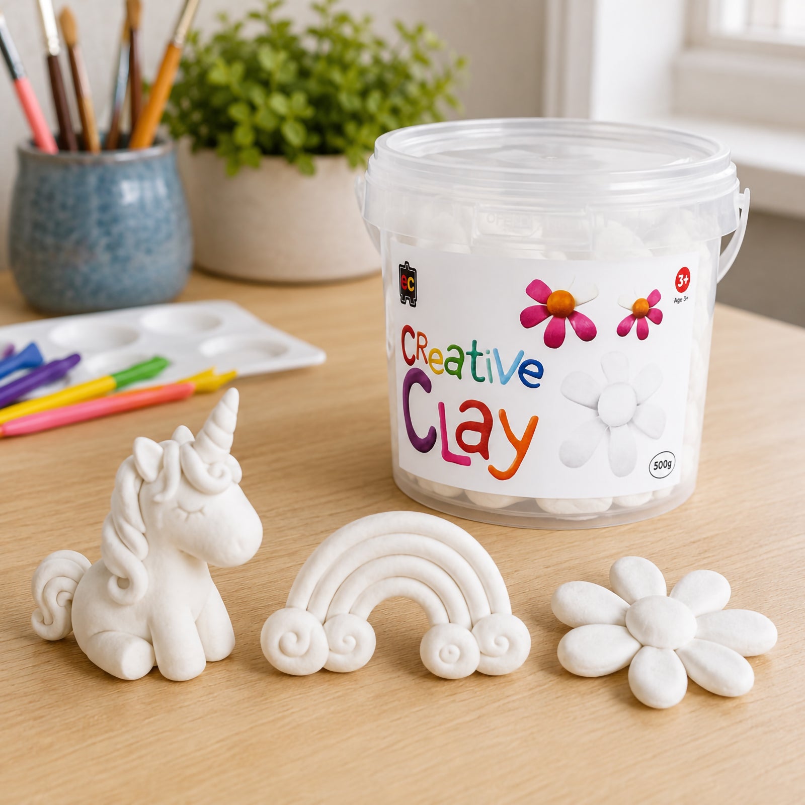 CreativeClay White 500g tub surrounded by detailed handcrafted clay creations including a unicorn, rainbow and flower. The image showcases the versatility of the clay for fantasy themed projects, decorative sculptures and advanced creative activities.