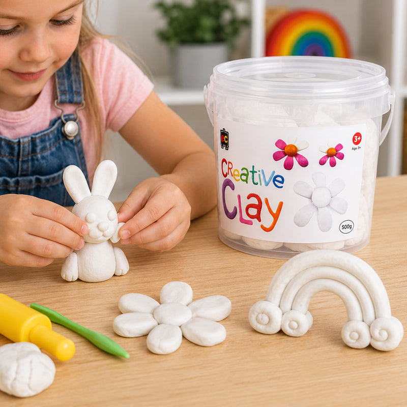 Young child creating a white clay rabbit beside a large 500g tub of Educational Colours CreativeClay. The scene includes handmade clay flowers, a rainbow sculpture and modelling tools, demonstrating the clay's suitability for educational activities, sensory learning and imaginative craft projects.