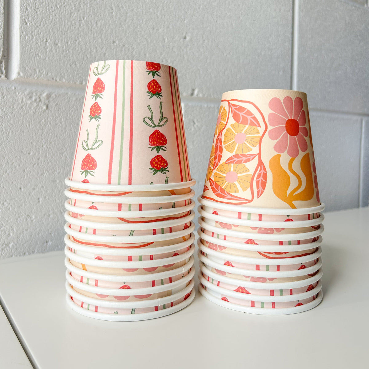 Two stacks of Creative Cafe Co 8oz printed takeaway cups in red and orange designs against a white wall