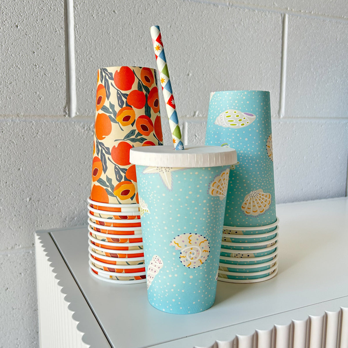 Creative Cafe Co 16oz printed takeaway cups with a cold lid and paper straw in front of stacked cups