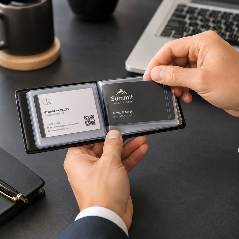 Professional hands browsing through a Cumberland Business Card File displaying neatly organised business cards on a modern executive desk beside a laptop, notebook and coffee cup, demonstrating quick access to important contacts during meetings.