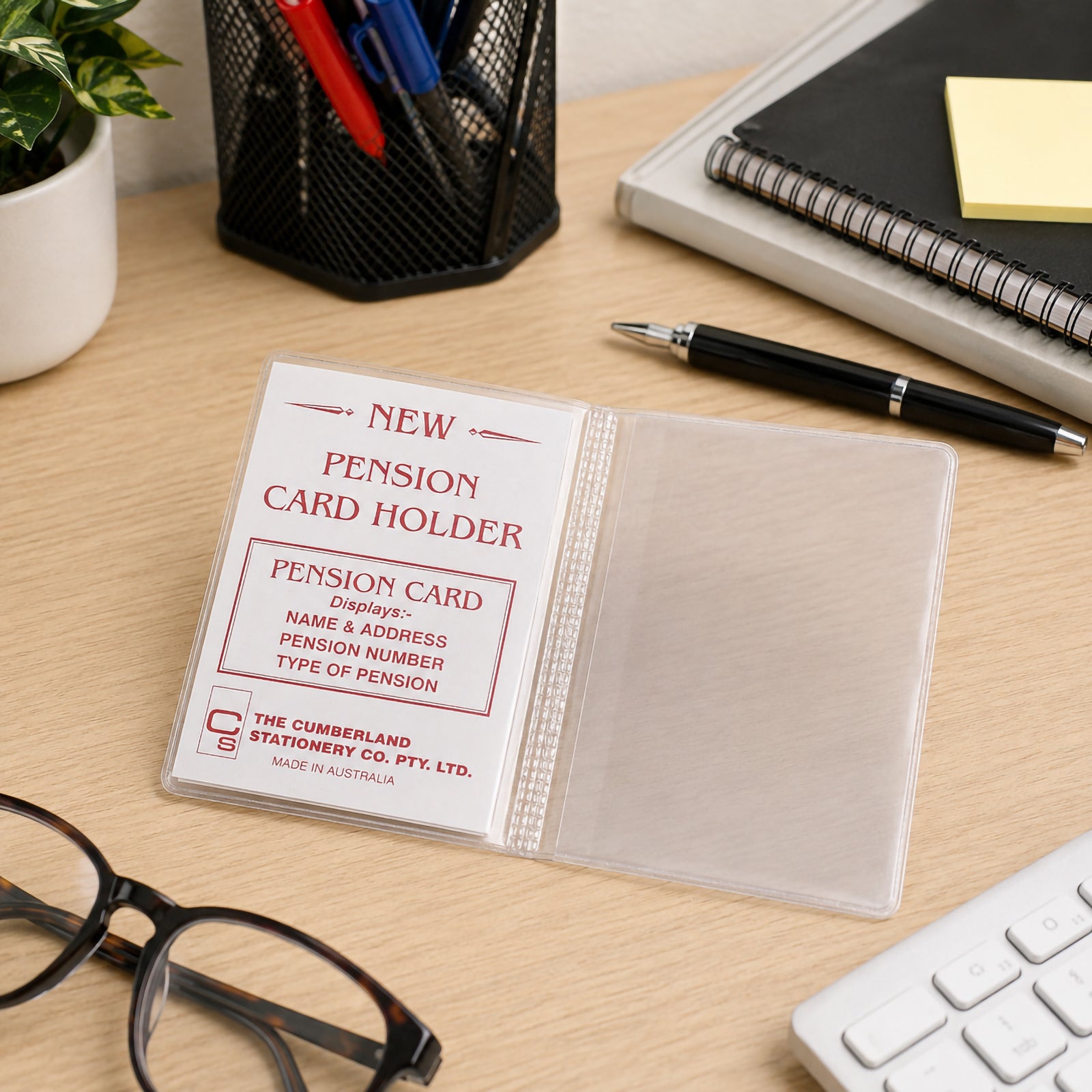 The Cumberland clear PVC card holder is displayed open on an organised office desk beside glasses, stationery and notebooks. A sample pension card insert illustrates how important cards remain protected while easily readable through the transparent PVC.