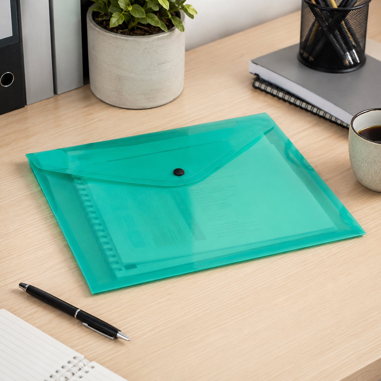 Cumberland A4 transparent green document wallet resting on a contemporary office desk with notebooks, stationery, coffee and filing folders, demonstrating a professional filing solution for everyday paperwork.