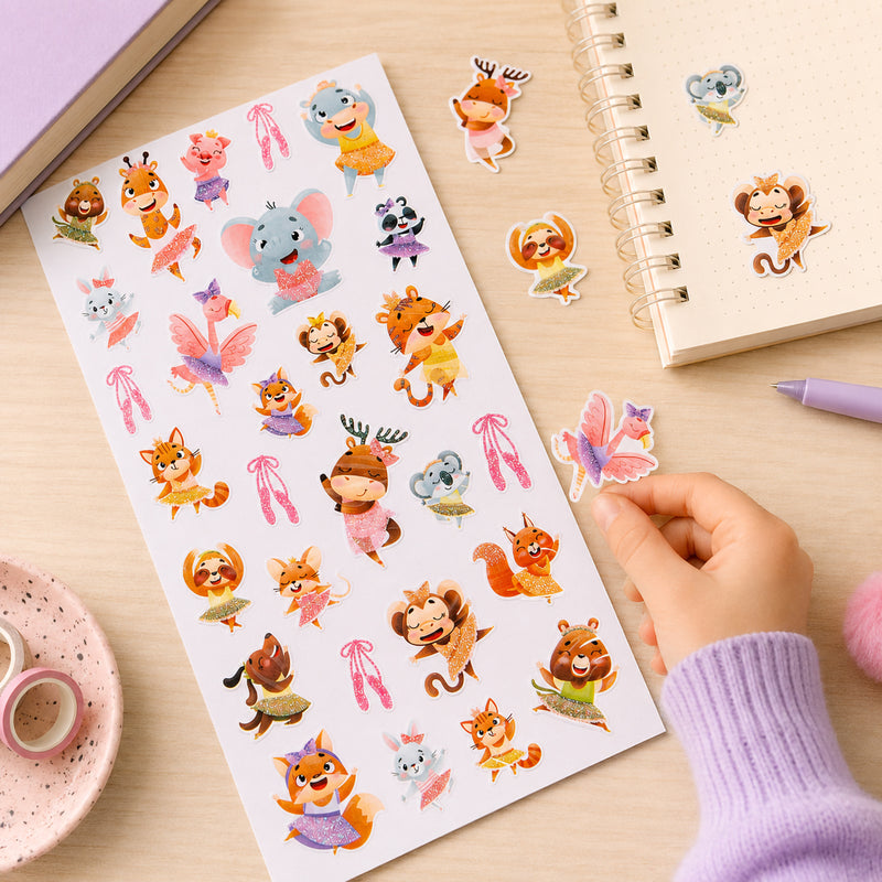 Child placing a glitter flamingo dancer sticker onto a notebook while surrounded by colourful animal dance stickers. The collection features cheerful animals wearing sparkling costumes and ballet themed accessories.