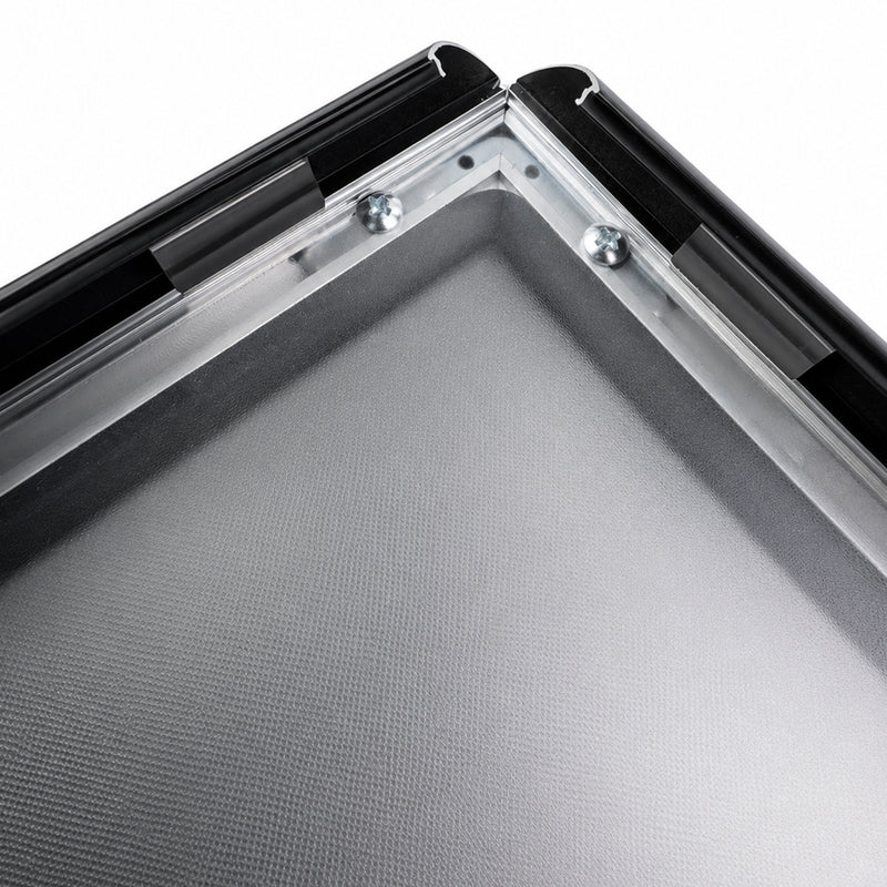 Close-up of the black snap frame corner with two sides hinged open, showing the aluminium profile, the clear cover sheet and the dark gasket seal running along the inner edge of the frame.