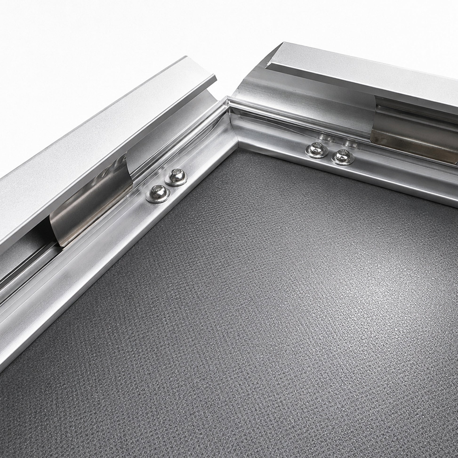 Close-up of the silver snap frame corner with the 32mm aluminium profile hinged open, showing the polished inner lip, the clear cover sheet and the rivets that hold the spring hinge.