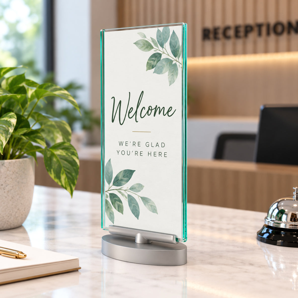 Deflecto DL portrait double sided rotating sign holder presenting a welcome message on a modern reception counter. The narrow clear display has polished green tinted edges and a silver freestanding