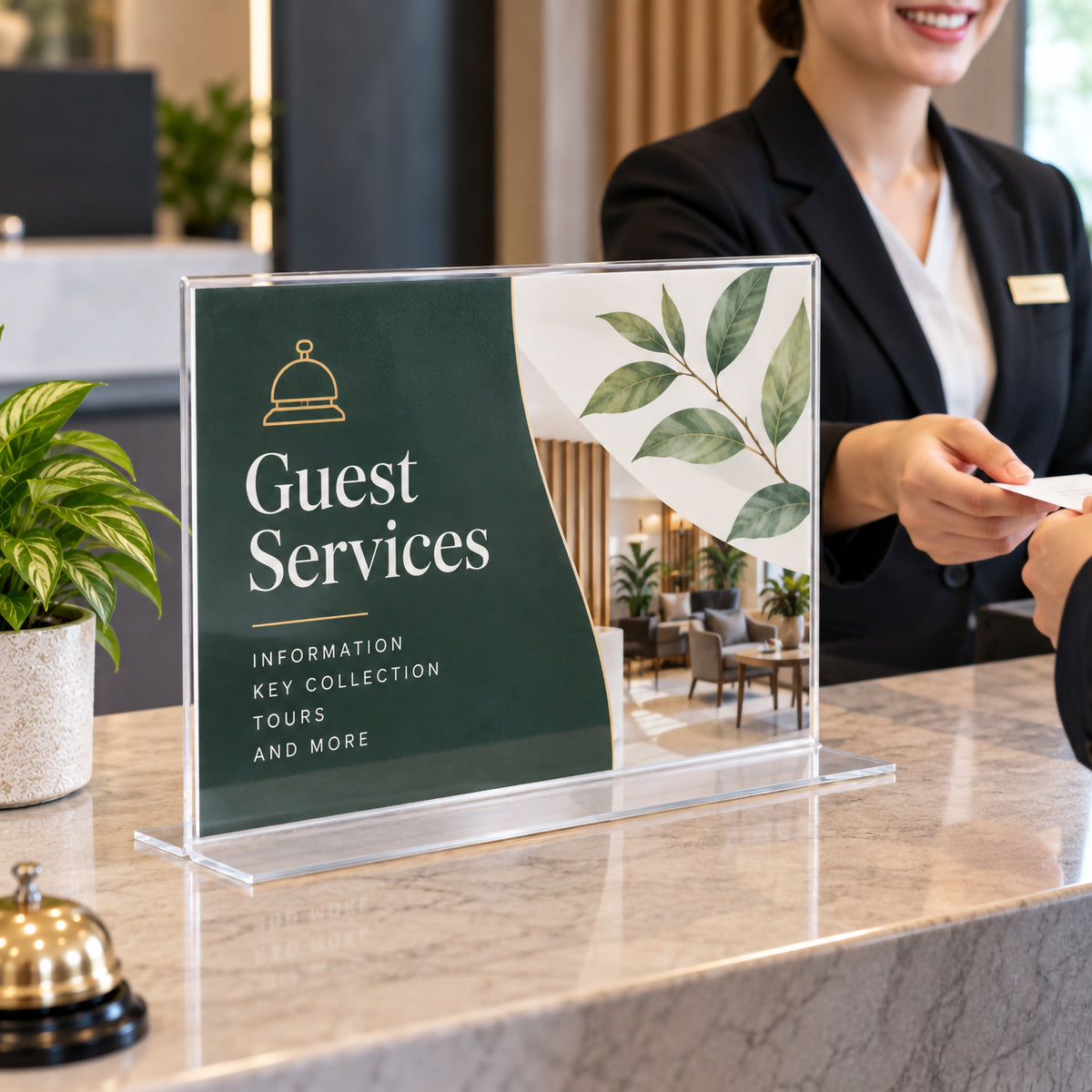 Deflecto A3 landscape double sided T shape sign holder displayed on a hotel reception counter with guest services information. The large clear freestanding holder presents prominent visitor messaging while a receptionist assists a guest, demonstrating its suitability for professional hospitality and customer service environments.