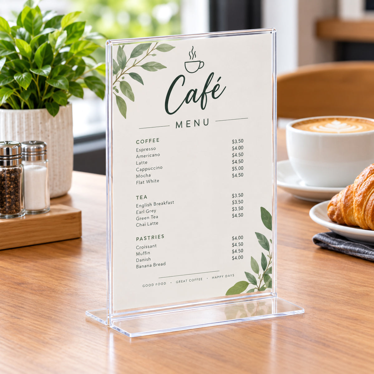 Deflecto A5 portrait T shape sign holder presenting a cafe menu on a timber table beside coffee, a croissant and table accessories. The upright clear display demonstrates how menus, prices and hospitality information can be presented neatly while occupying a compact area of valuable tabletop space.