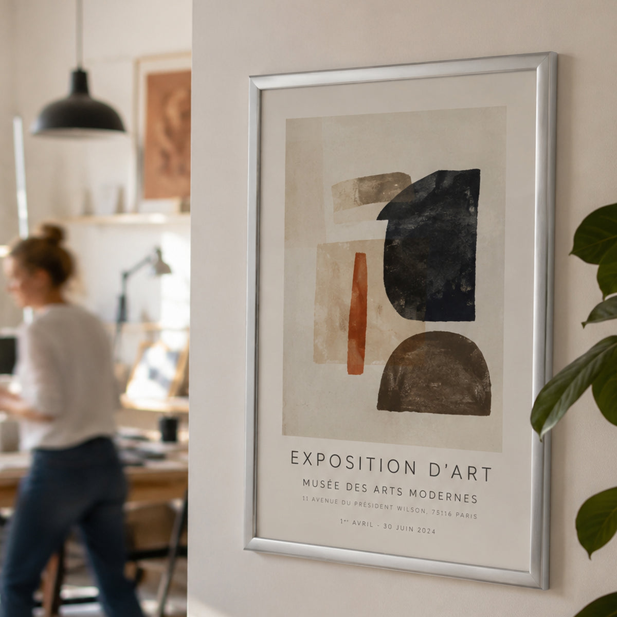 Deflecto A2 silver picture and certificate frame on a studio wall displaying an abstract art print, with people working nearby