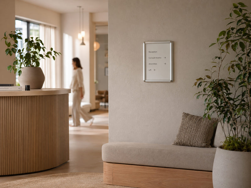 Deflecto A4 silver rounded edge snap frame mounted on a wall in a bright reception area beside a curved timber counter