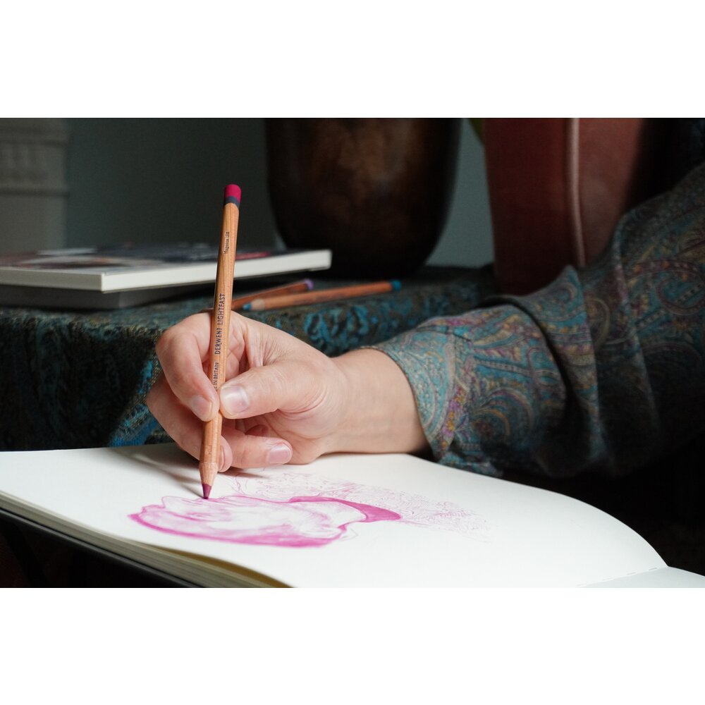 Close view of a hand shading a pink sketch in a pad with a Derwent Lightfast pencil, a Derwent range image showing the pencils in use
