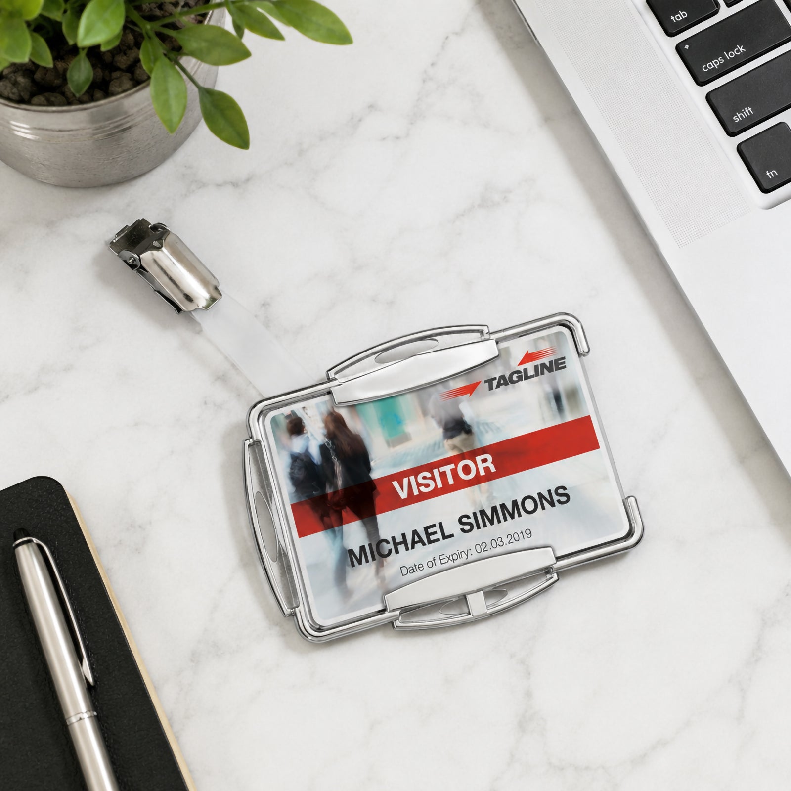 Top view of the Durable RFID Secure Mono Card Holder placed on a marble office desk beside a laptop, notebook, pen and potted plant. The image highlights the rotating clip attachment, professional silver finish and compact design for secure identification management.