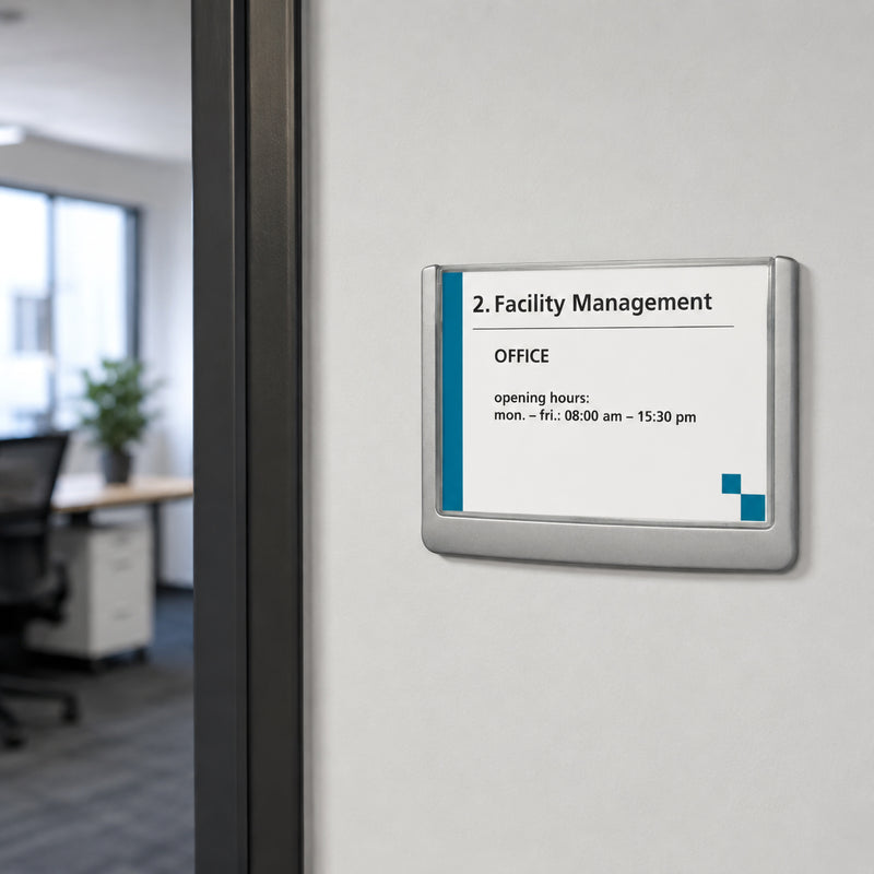 The Durable Click Sign 149 x 105.5mm Grey mounted neatly beside a modern office doorway. The sleek grey frame is installed on a clean white wall with a contemporary workspace visible in the background, illustrating its use for room identification and professional office signage.