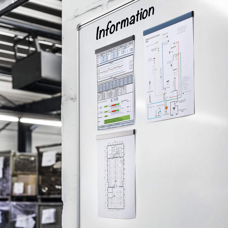 Dark blue Durable Durafix magnetic strips installed on an information board in an industrial environment displaying reports, wiring diagrams and floor plans. The image highlights their suitability for warehouses, manufacturing facilities and operational workplaces.