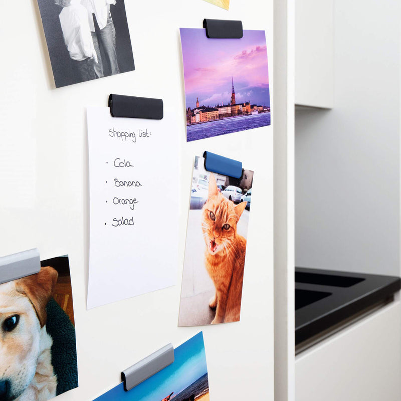 Side angle of assorted magnetic clips mounted on a refrigerator door holding photographs and a handwritten shopping list. The different coloured clips demonstrate attractive colour coding while keeping documents securely displayed and easy to update.