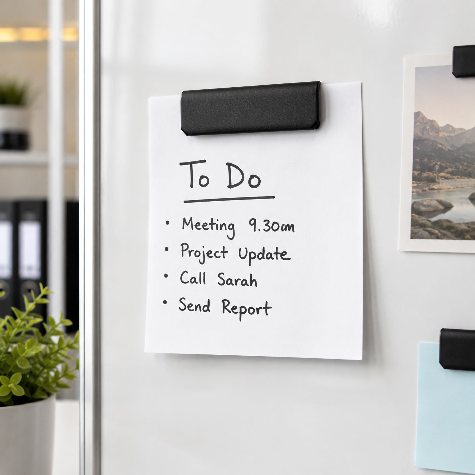 A black Durable Durafix Magnetic Clip holds a handwritten to do list on a white magnetic cabinet in a modern office. Nearby stationery and office accessories reinforce its practical use for organising daily tasks and workplace reminders.