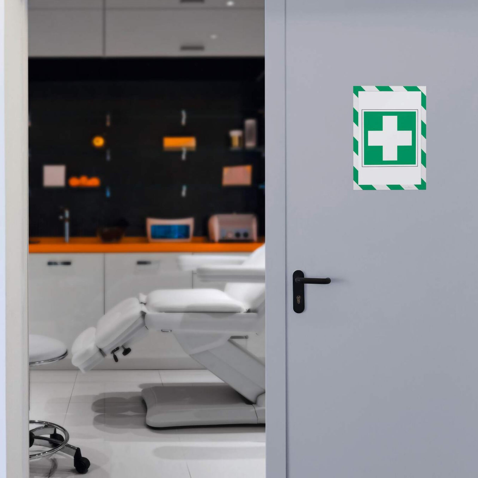 Durable DURAFRAME Magnetic Security A4 Green White frame displayed on a medical treatment room door featuring a first aid cross sign. The frame clearly identifies emergency facilities while maintaining a clean professional appearance.