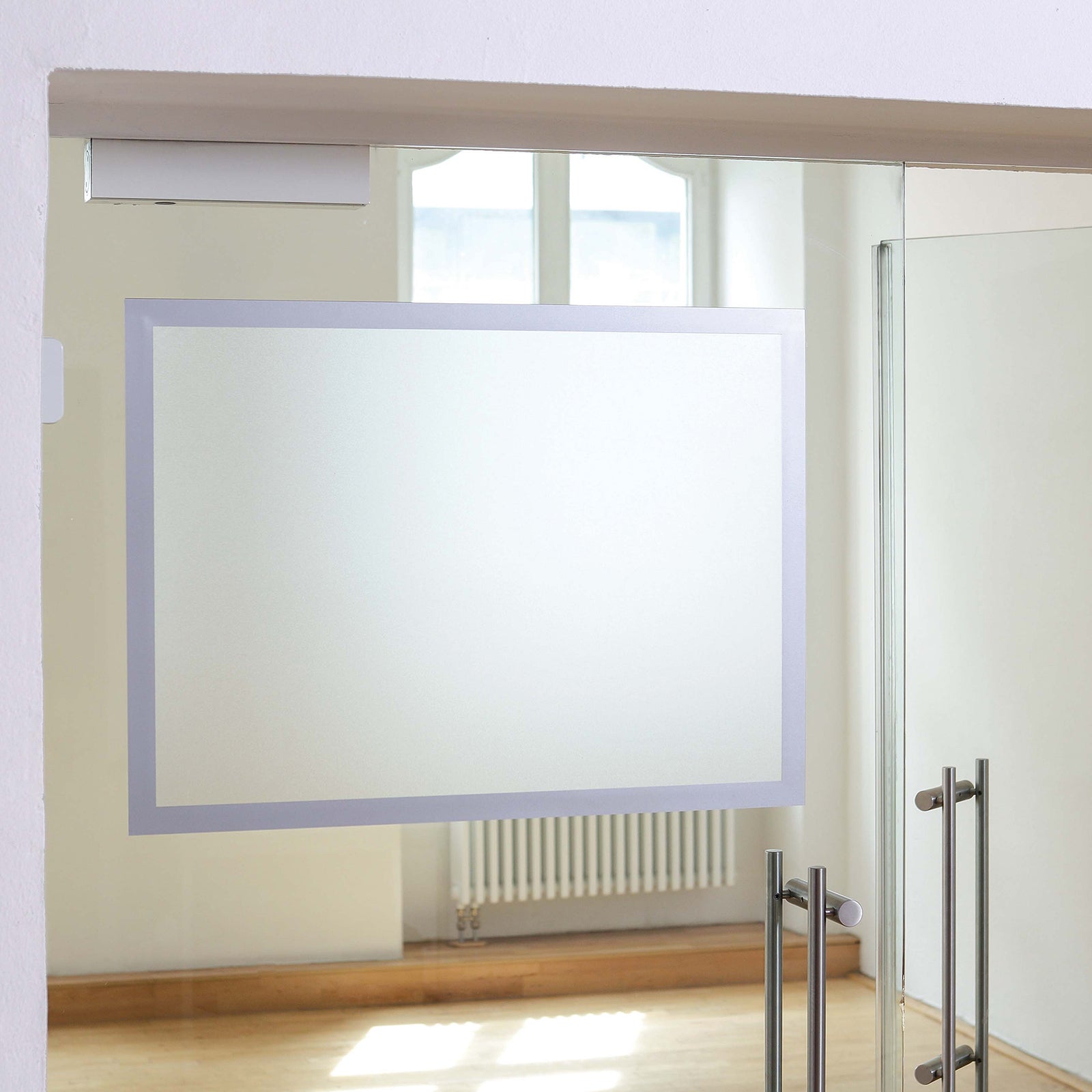 The Durable DURAFRAME Poster A2 Silver installed on a glass entrance with no poster inserted, highlighting the clean silver magnetic border and transparent display area ready for quick insertion of promotional or informational documents.