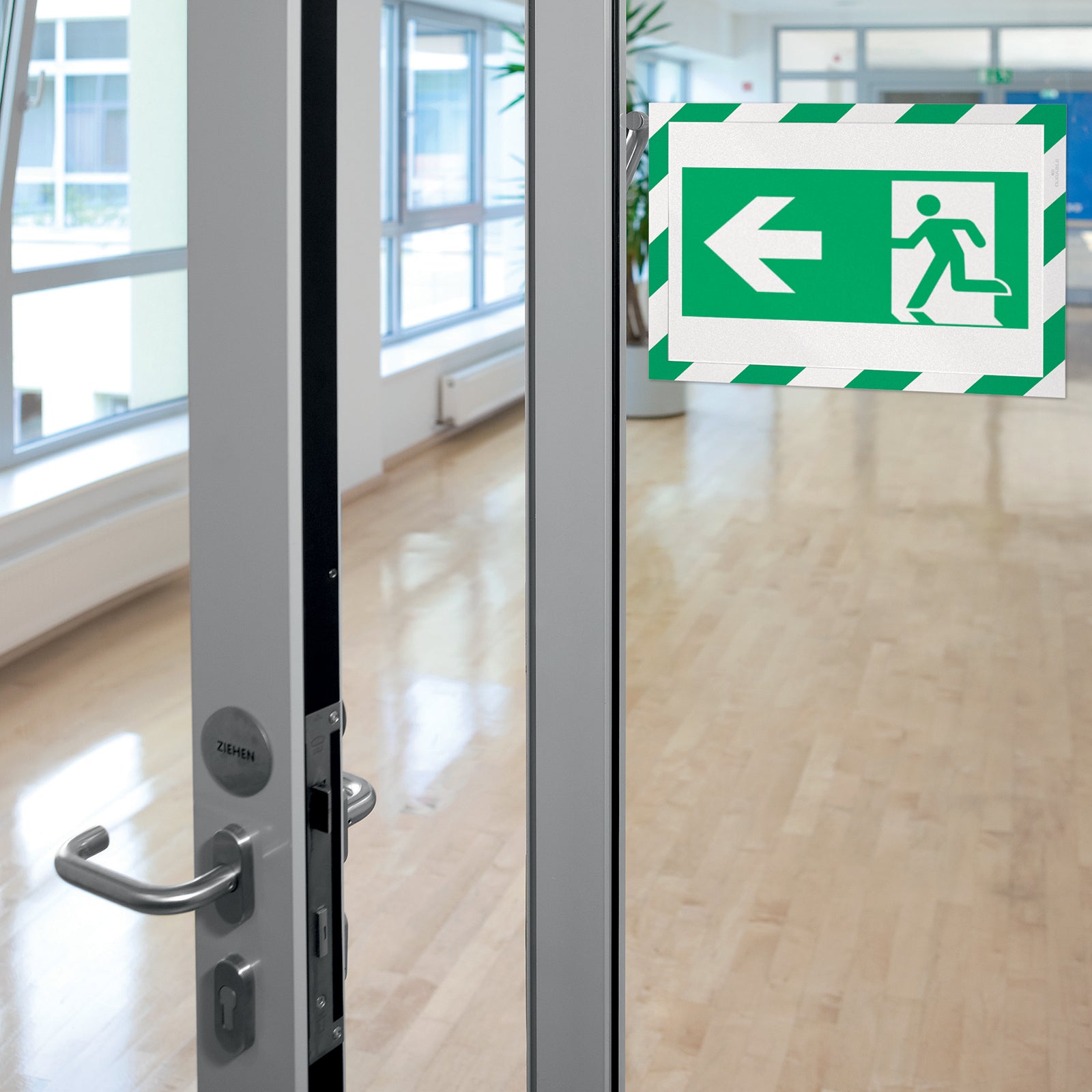 Durable DURAFRAME Security A4 Green White mounted on a modern glass entrance displaying an emergency exit sign. The professional frame provides excellent visibility while complementing contemporary commercial interiors.