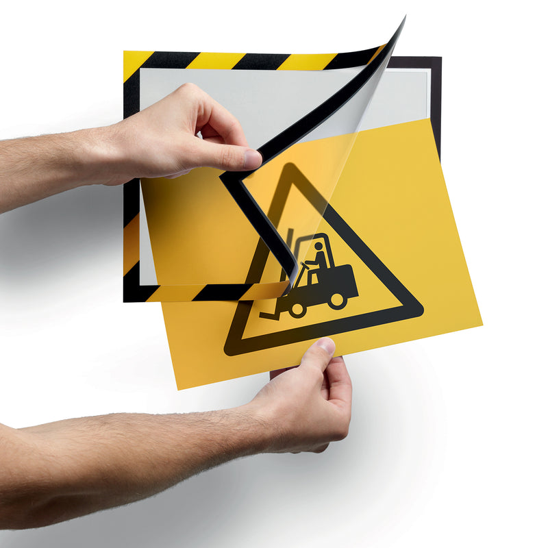 Hands lifting the magnetic front of the Durable DURAFRAME Security frame to insert or replace a forklift warning document. The fold back design enables fast updates without removing the frame from the surface.