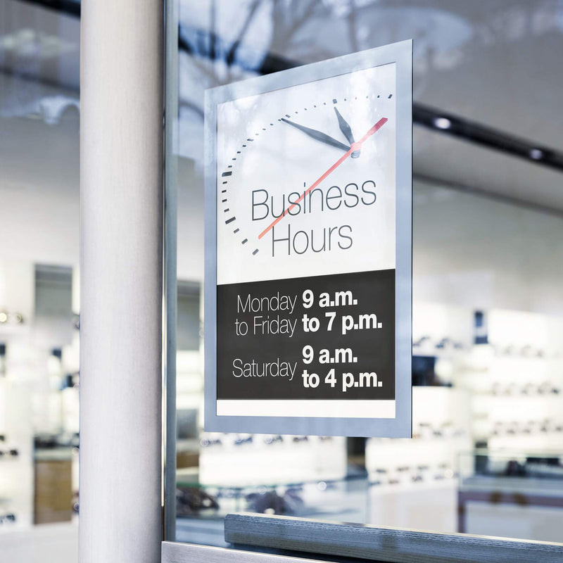 Durable DURAFRAME Sun A4 Silver mounted on a glass window showing business hours in a bright retail environment. The image highlights double sided visibility, clean glass presentation and suitability for shopfront communication.