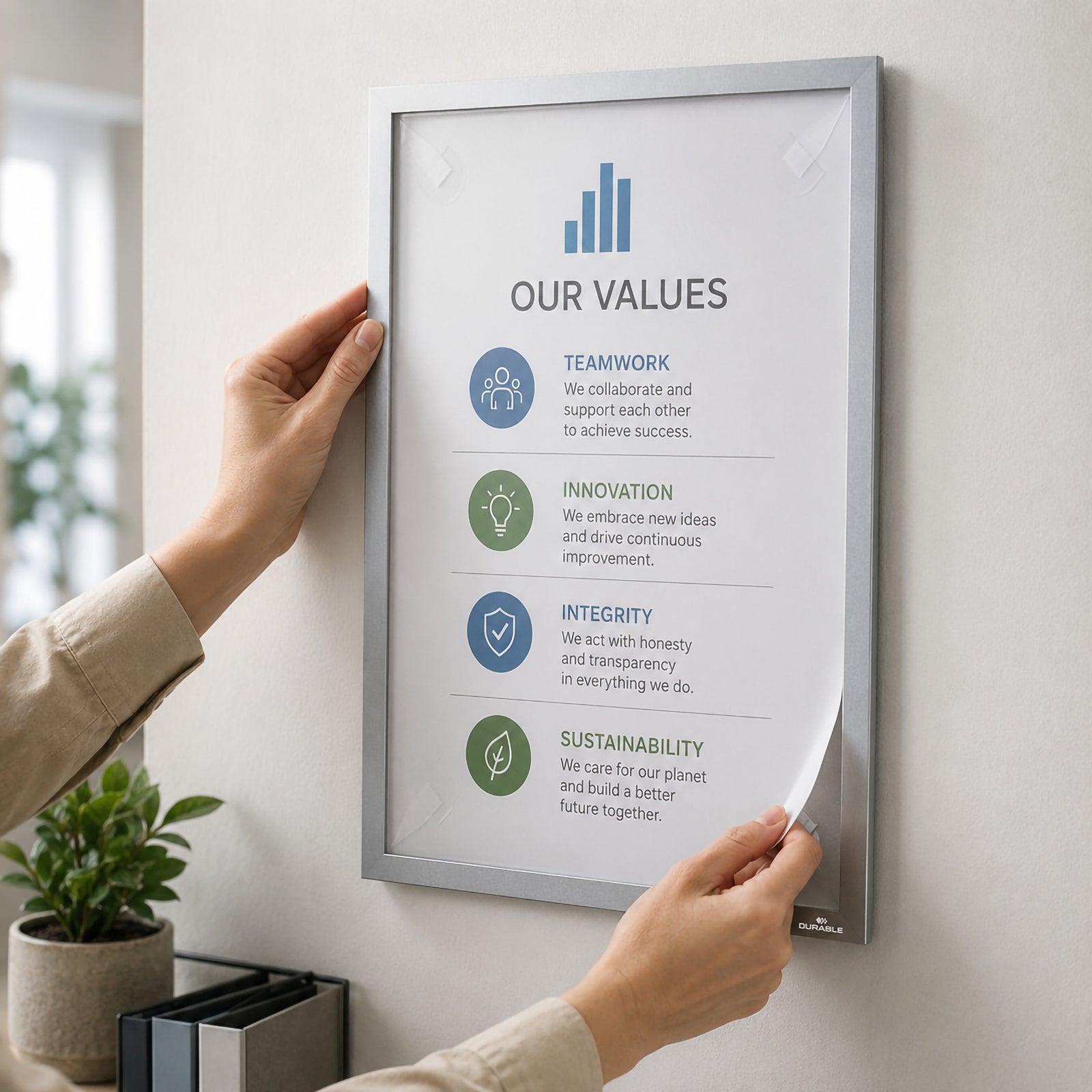 Hands applying the Durable DURAFRAME Wallpaper A3 Silver to a painted office wall while replacing an information sheet through the fold back magnetic frame. The image demonstrates quick document changes, secure mounting and clean professional presentation without damaging delicate wall surfaces.