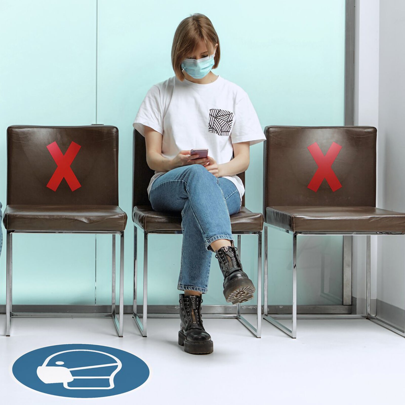 Waiting room with Durable Cross X Red markers attached to unused chairs, helping visitors maintain appropriate seating separation while a masked occupant sits in the designated available seat.