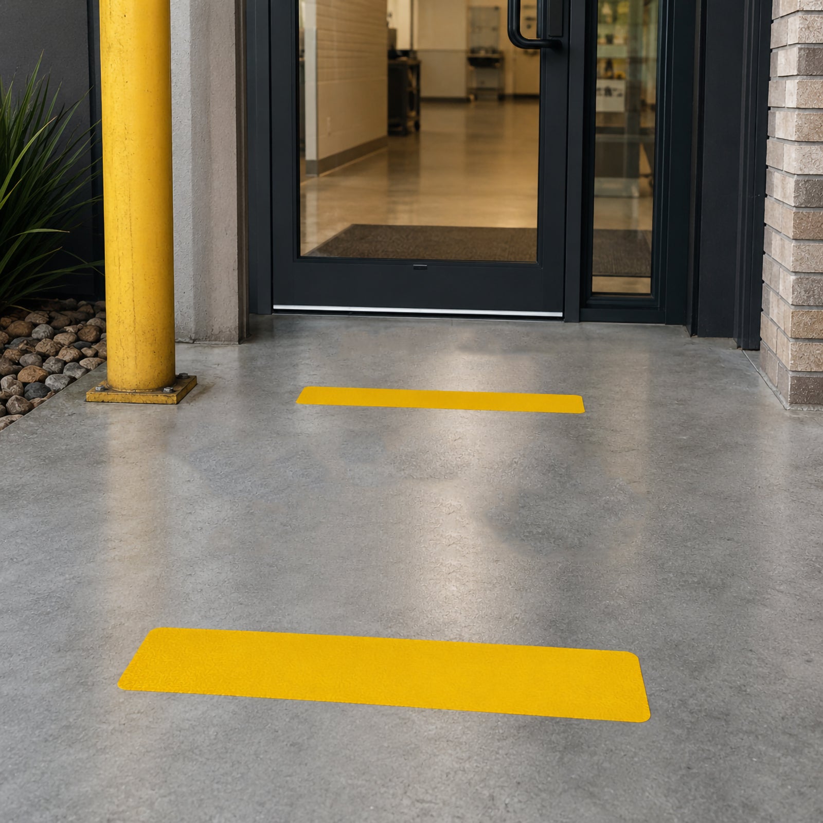 Close up of a Durable Floor Marking Stripe Yellow applied at the entrance to an industrial building, providing a clear visual boundary on a clean concrete floor beside protective safety bollards.