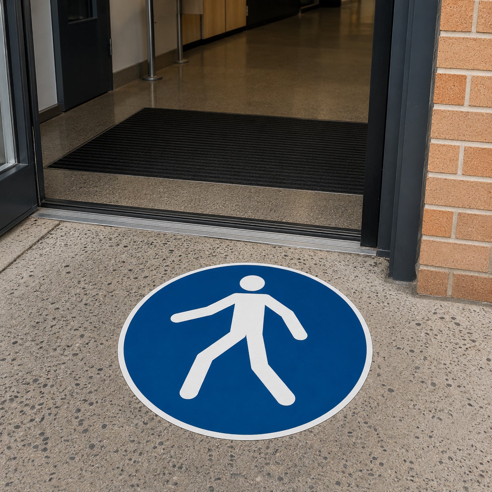 The Durable Floor Marking Sign Use Walkway 430mm Blue positioned at the entrance to a commercial building, directing staff and visitors to follow the approved pedestrian route before entering the workplace.