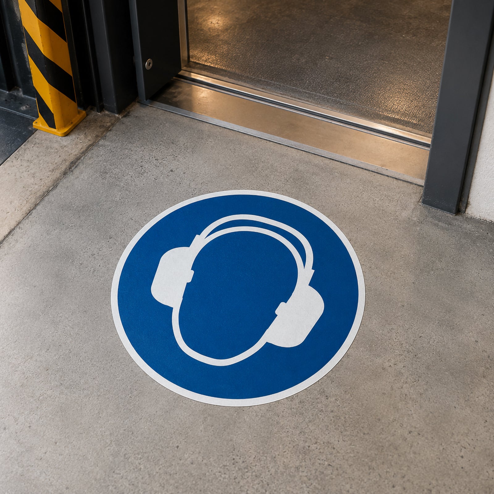 The Durable Floor Marking Sign Use Ear Protection 430mm Blue positioned at the entrance to an industrial workspace, reminding employees and visitors to wear hearing protection before entering a designated high noise area.