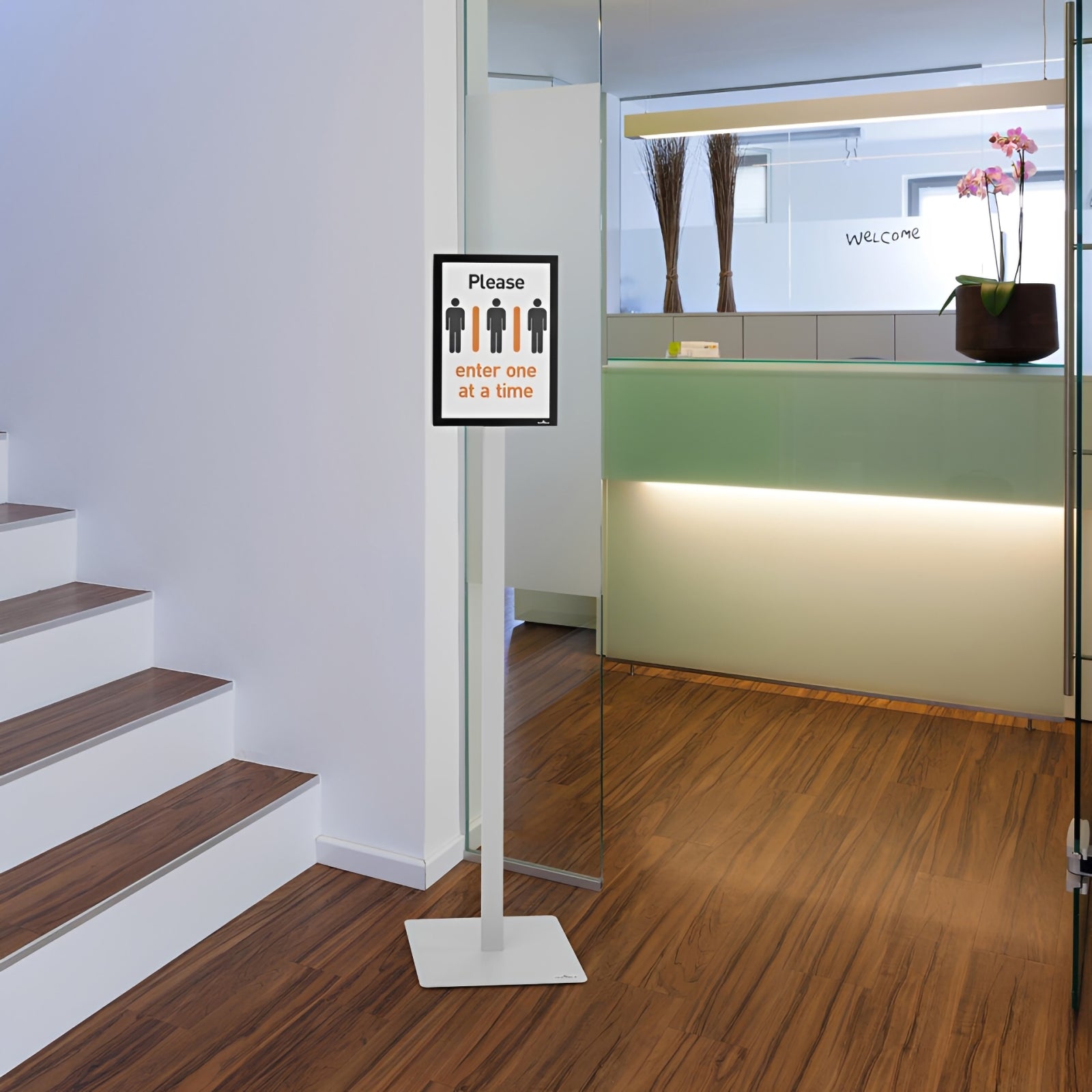 The Durable Info Stand Floor Basic A4 Silver positioned at the entrance of a modern office reception displaying an entry guidance notice. Its slim profile and stable weighted base make it ideal for directing visitors in professional environments.