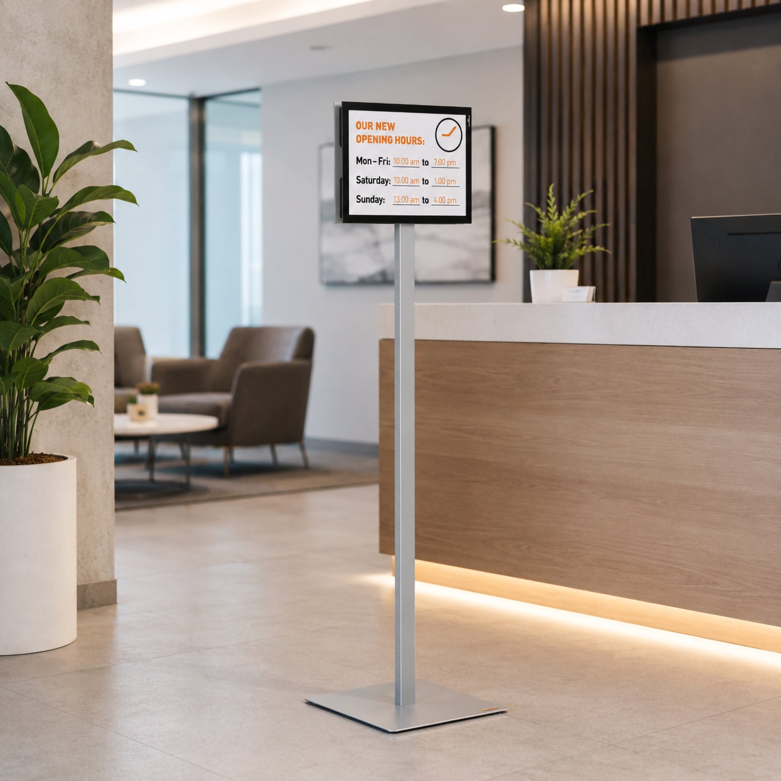 Lifestyle image showing the Durable Info Stand Floor Basic A4 Silver positioned beside a professional reception counter displaying business opening hours. The premium aluminium stand creates a welcoming first impression while clearly communicating important visitor information.