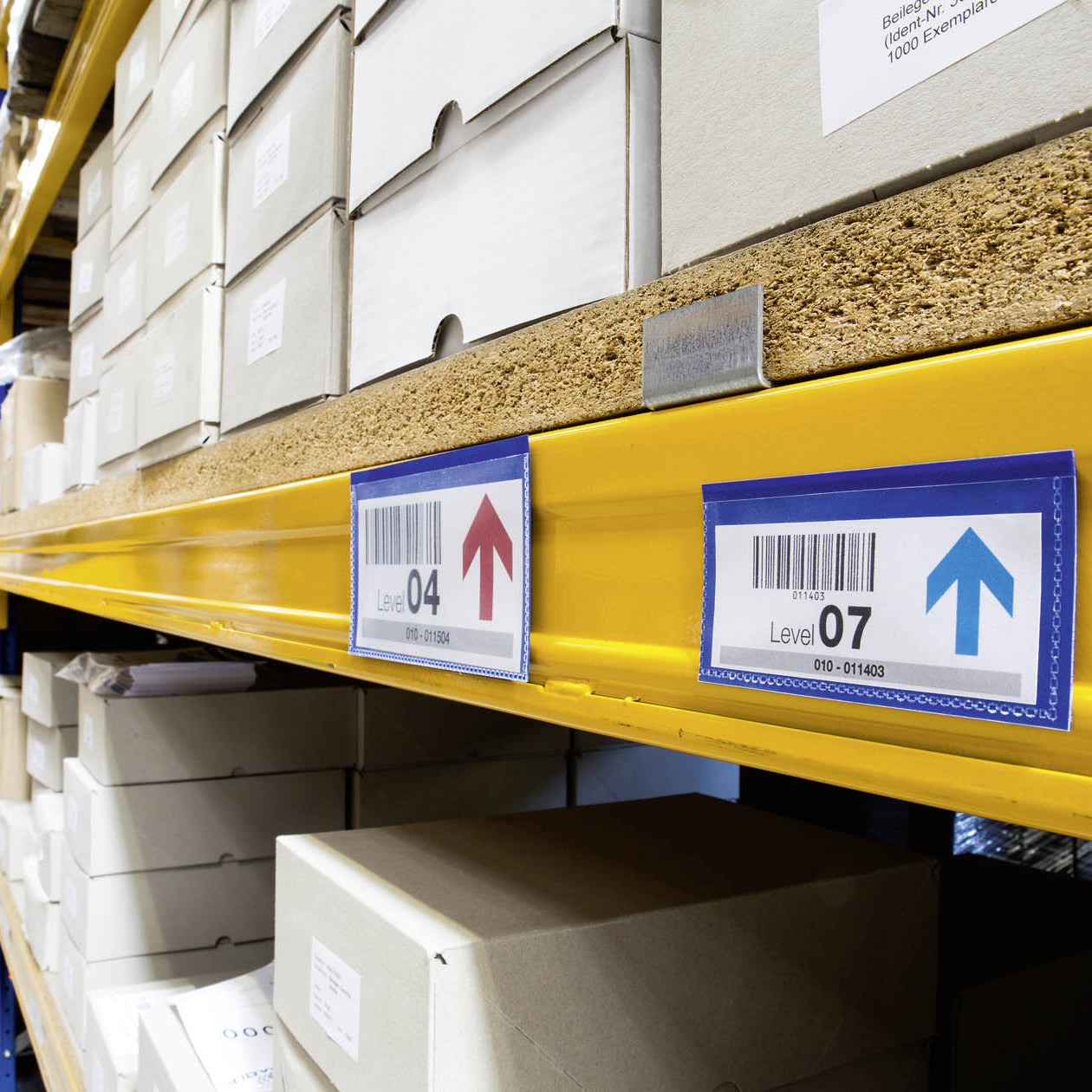 Multiple Durable Magnetic Document Pouches mounted along industrial warehouse shelving displaying barcode location labels. The image highlights their use for organised stock identification, inventory control and efficient warehouse navigation.