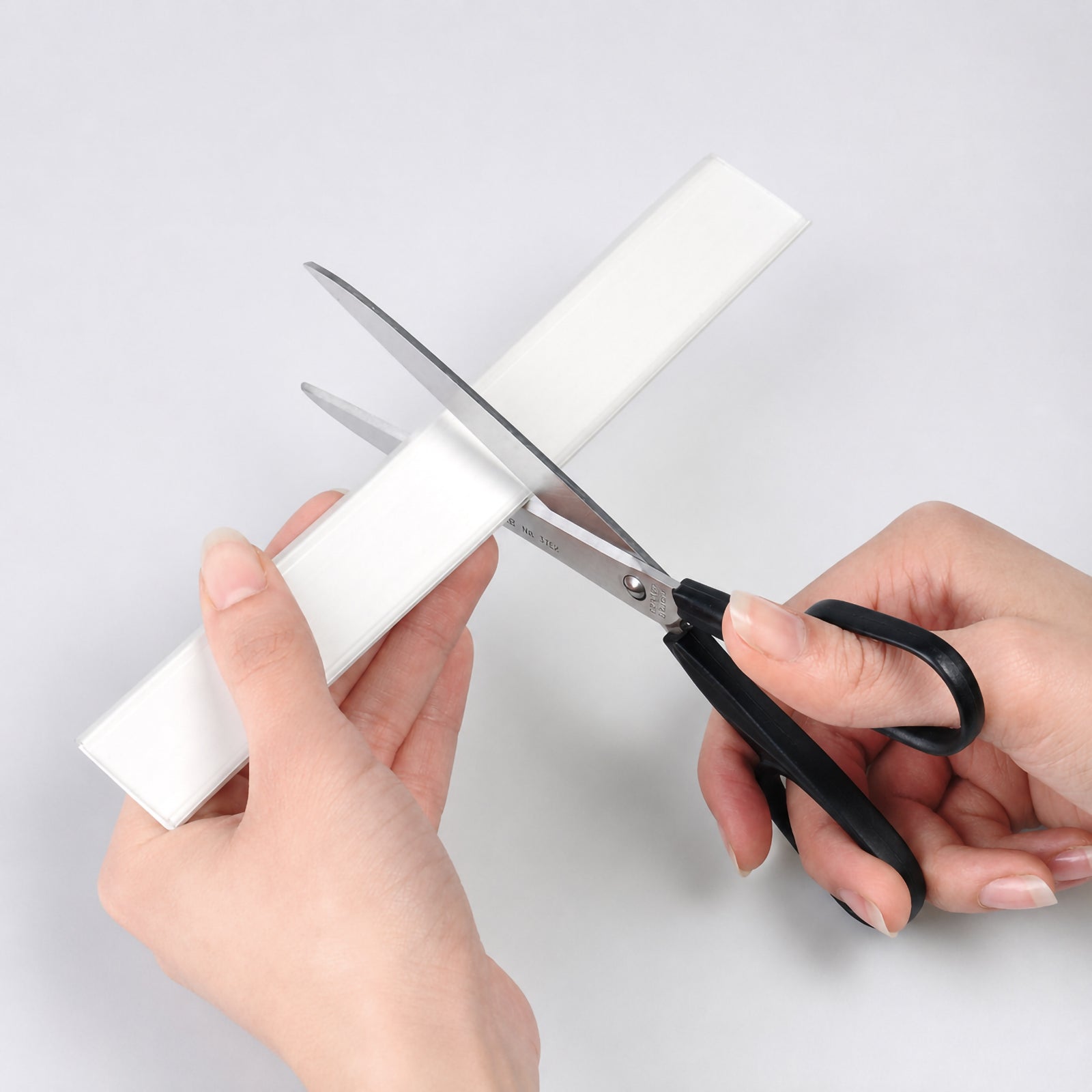 Close up of the Durable Scanfix Self Adhesive Label Strip being trimmed with scissors, demonstrating how the transparent plastic rail can be easily cut to the required length for customised shelf labelling applications.